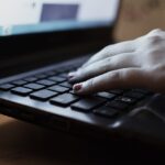 Hands typing on a laptop keyboard at a desk — draft editing and copy polish workspace