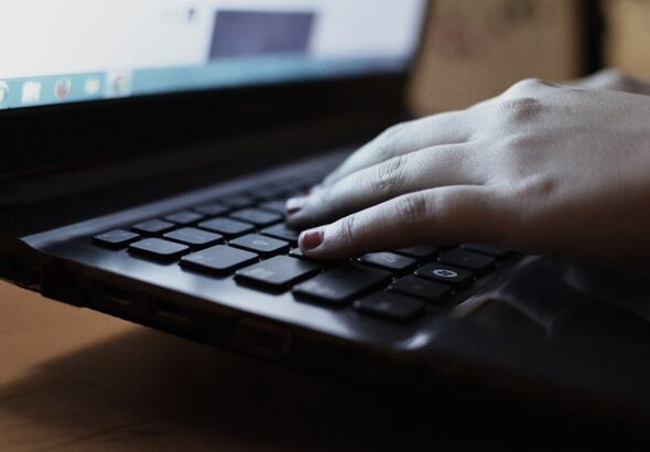 Hands typing on a laptop keyboard at a desk — draft editing and copy polish workspace