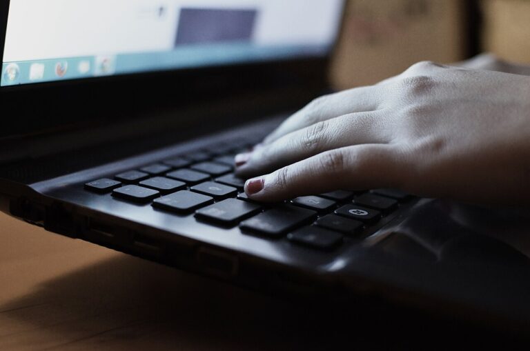 Hands typing on a laptop keyboard at a desk — draft editing and copy polish workspace