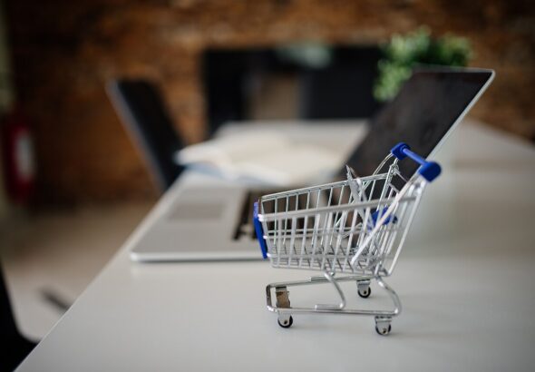 Mini shopping cart beside a laptop — ecommerce product listings