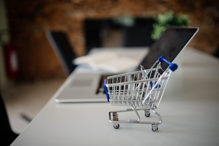 Mini shopping cart beside a laptop — ecommerce product listings