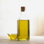Corked glass bottle of golden olive oil next to a small glass bowl of oil