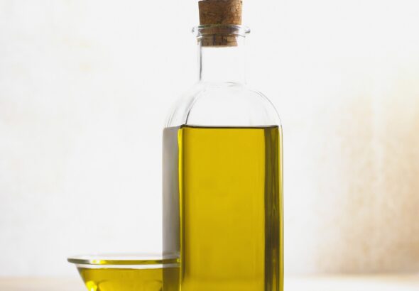 Corked glass bottle of golden olive oil next to a small glass bowl of oil