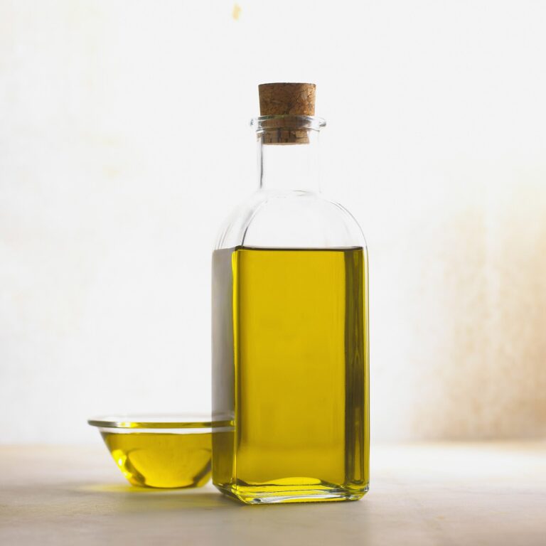 Corked glass bottle of golden olive oil next to a small glass bowl of oil