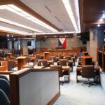 Empty Philippine Senate session hall with desks, lecterns and the Philippine flag behind the presiding officer's rostrum