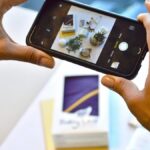 Hands taking a smartphone photo of a product flat lay on a white table for an online shop listing
