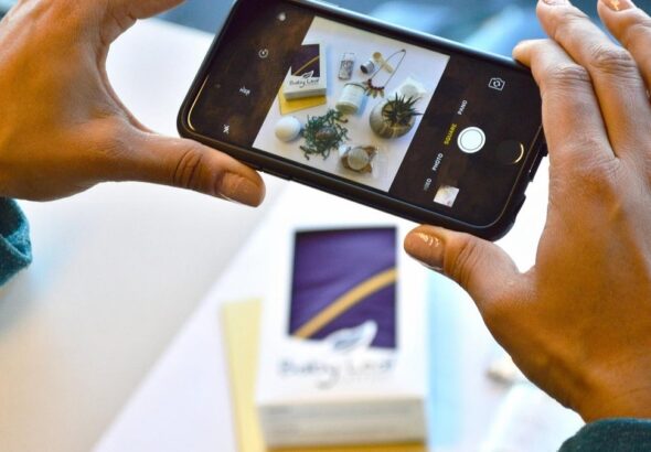Hands taking a smartphone photo of a product flat lay on a white table for an online shop listing