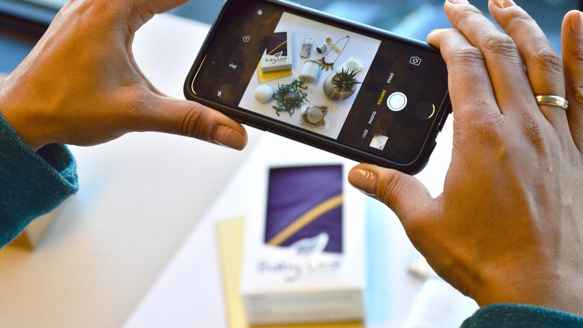 Hands taking a smartphone photo of a product flat lay on a white table for an online shop listing