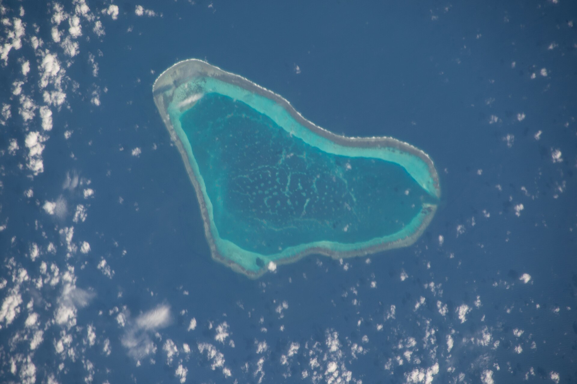 Aerial view of Scarborough Shoal (Bajo de Masinloc), a triangular coral reef ring with a turquoise lagoon in dark blue sea