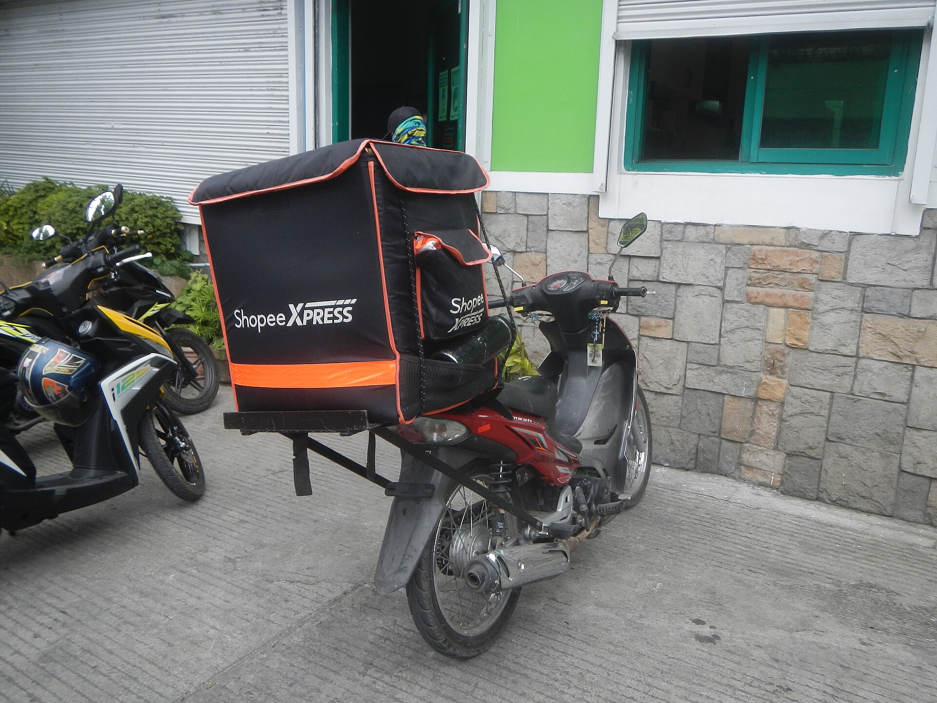 Shopee Xpress delivery motorcycle with a black and orange cargo box parked outside a building in the Philippines